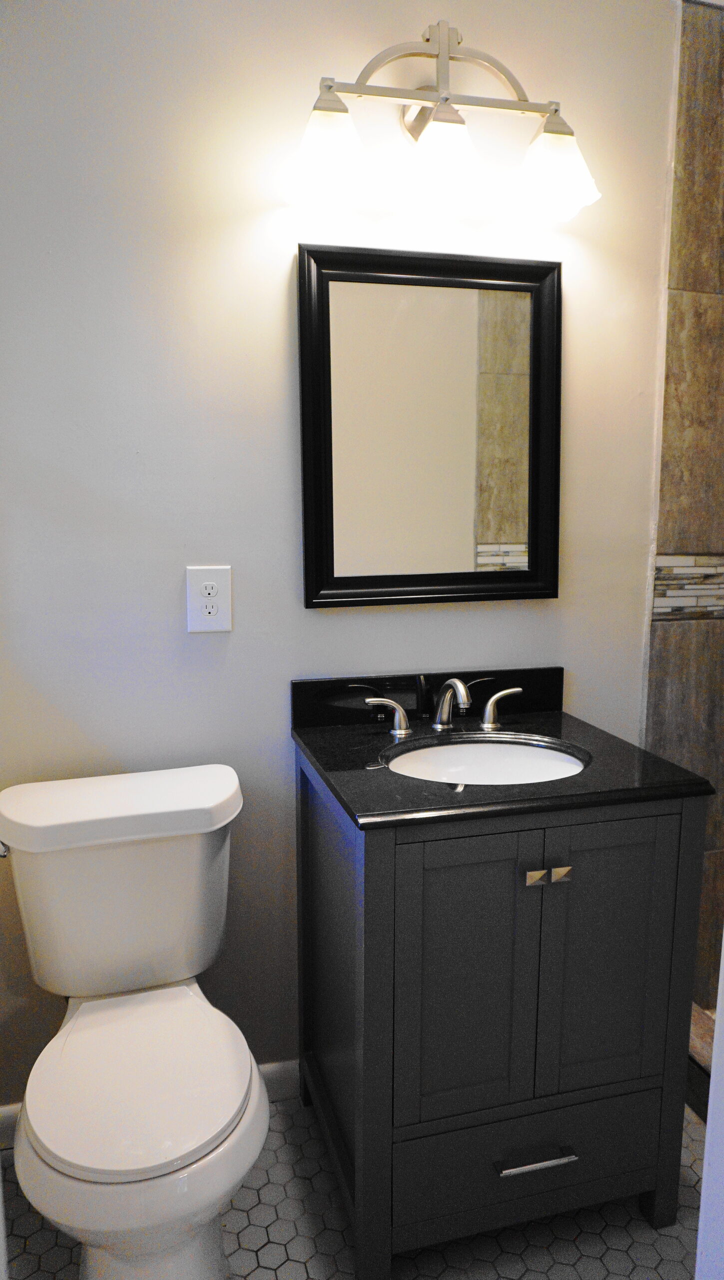 Powder room renovation Atlanta GA — dark vanity, framed mirror, sconce lighting